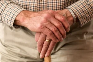 An elderly man holding a walking stick in a close-up view, highlighting his aged hands.