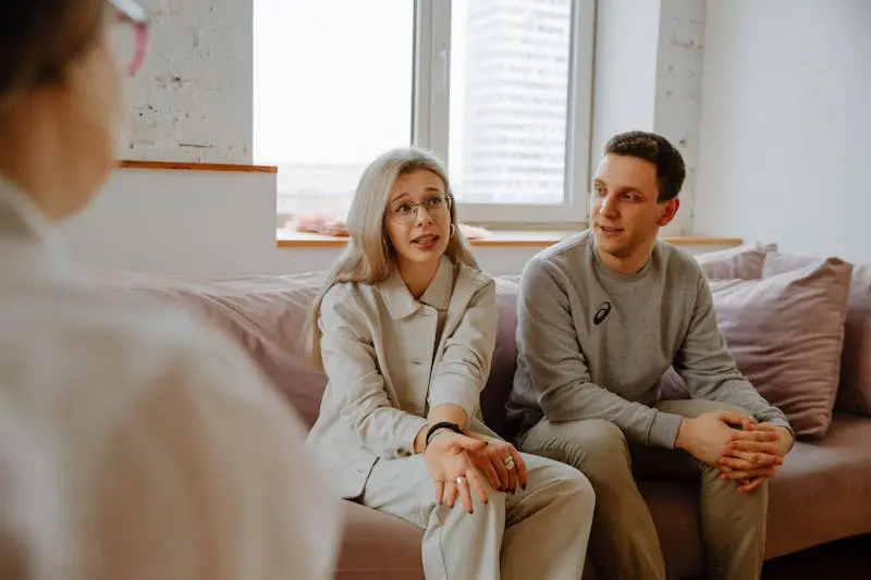 A man and woman are seated on a couch, having a discussion with each other.